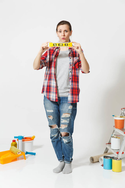 Full length of woman with building bubble spirit level standing near instruments for renovation apartment home isolated on white background. Wallpaper, accessories for gluing, tools. Repair concept. - Fotografie, Obrázek