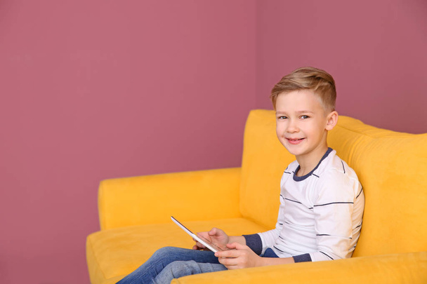Cute little boy sitting on sofa with tablet computer, indoors - Fotoğraf, Görsel
