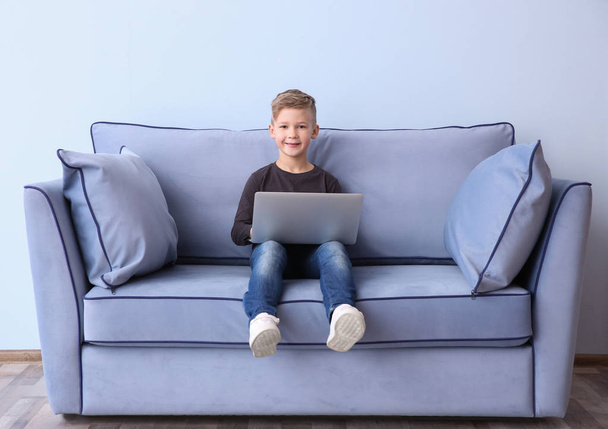 Cute little boy with laptop sitting on sofa, indoors - Foto, Bild