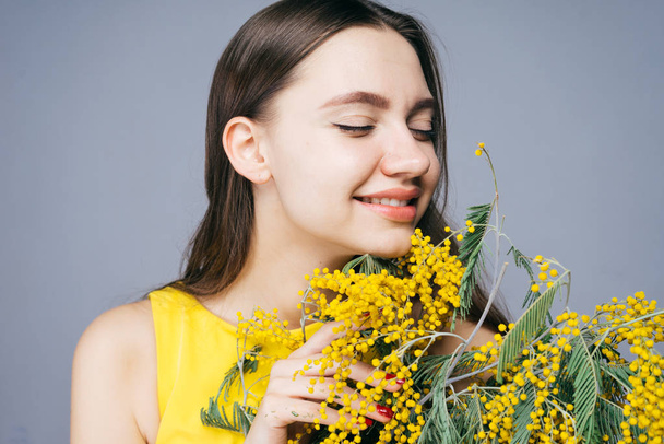 happy smiling girl in a yellow dress smelling a fragrant yellow mimosa - Photo, image