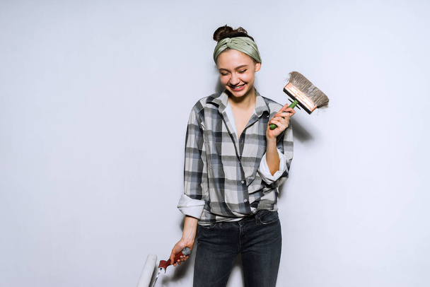 riéndose jovencita haciendo reparaciones en su apartamento, sosteniendo cepillo y rodillo en las manos
 - Foto, imagen