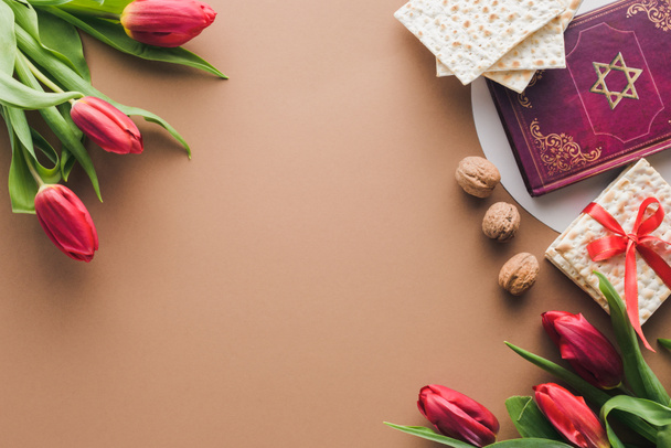 верхний вид традиционной книги с текстом на иврите, букеты красных тюльпанов и маца на столе
 - Фото, изображение