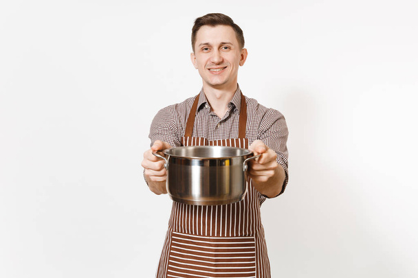 Man chef in striped brown apron holding silver stainless glossy aluminium empty stewpan, pan or pot isolated on white background. Male housekeeper or houseworker. Kitchenware, dishes, cuisine concept. - Photo, Image