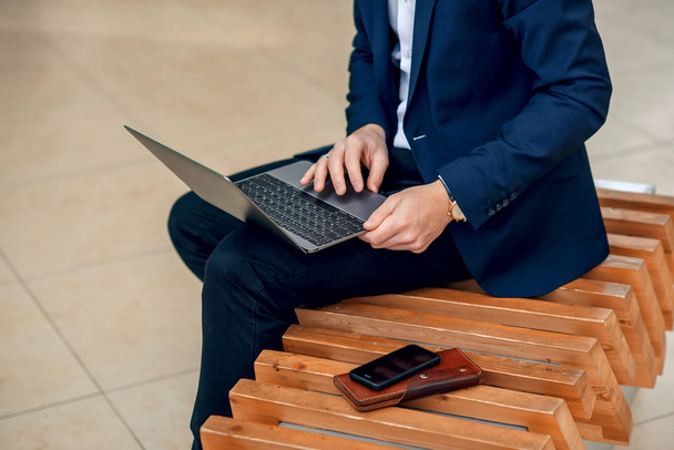 A businesswoman working on a laptop sitting on a bench, close up. Forex cryptocurrency trading, business concept. Leather wallet and smartphone on the branch. Selective focus. - Foto, afbeelding