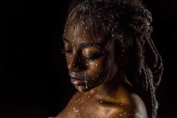 close-up view of seductive african american girl with milk drops on face and body isolated on black  - Фото, зображення