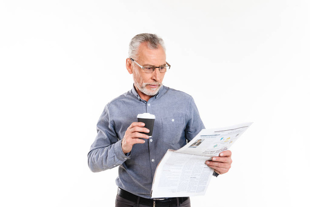 Old concentrated man holding coffee and reading newspaper isolated - Фото, изображение