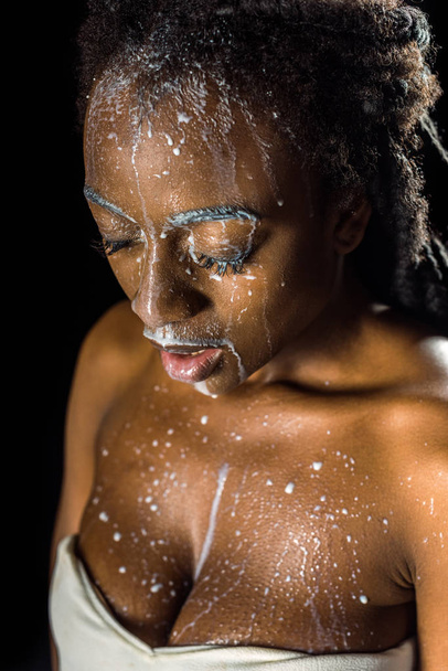 beautiful young african american woman with spilled milk on face isolated on black - Photo, Image