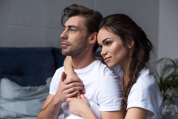 Young attractive couple hugging in bedroom and looking away - Fotografie, Obrázek