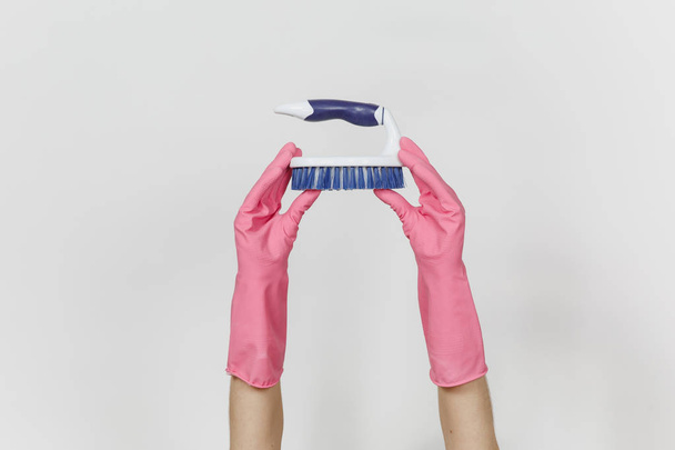 Close up van vrouwelijke handen in roze handschoenen horizontaal witte borstel met harde vezels houdt voor het reinigen met blauwe geïsoleerde op witte achtergrond. Schoonmaak leveringen concept. Ruimte voor advertentie kopiëren - Foto, afbeelding