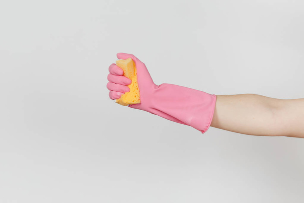 Close up of female hand in pink gloves holds and squeezes yellow-orange sponge for cleaning and washing dishes isolated on white background. Cleaning supplies concept. Copy space for advertisement - 写真・画像