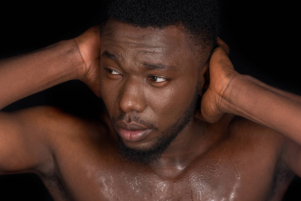 молодой потный африканский американец с голыми грудями закрывает уши руками и смотрит в сторону, изолированный от черного
 - Фото, изображение