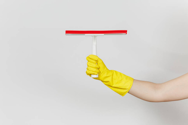 水平に白い背景に分離された赤の要素を持つ表面のクリーニングのための白いスキージが保持している黄色の手袋の女性の手のクローズ アップ。クリーニング用品の概念。広告のためのスペースをコピーします。 - 写真・画像