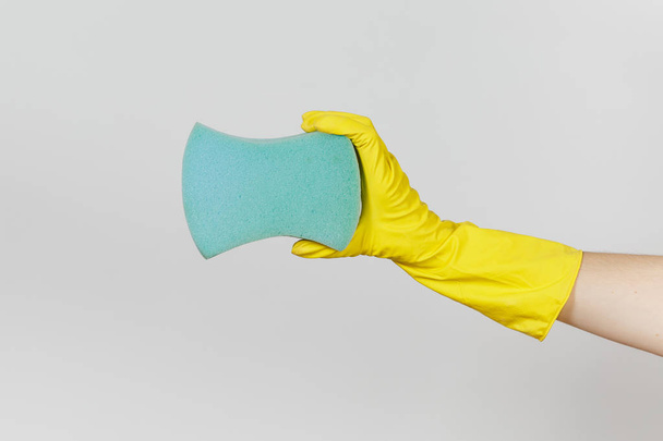 El primer plano de la mano femenina en guantes amarillos horizontales sostiene una gran esponja azul para limpiar y lavar los platos aislados sobre fondo blanco. Concepto de artículos de limpieza. Copiar espacio para publicidad
 - Foto, imagen