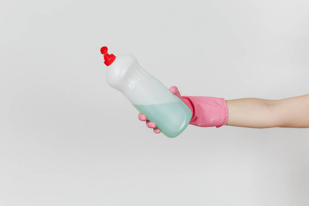 Zbliżenie ręka w różowe rękawiczki posiada wylać biały butelka z zielonym cleaner płyn do mycia naczyń z miejscem na tekst na białym tle. Czyszczenie koncepcji zaopatrzenia - Zdjęcie, obraz