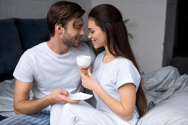 Ευτυχισμένο ζευγάρι με καφέ αγκαλιά στο κρεβάτι - Φωτογραφία, εικόνα