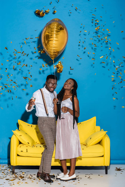 happy young african american couple holding glasses of champagne and golden balloon - Foto, afbeelding