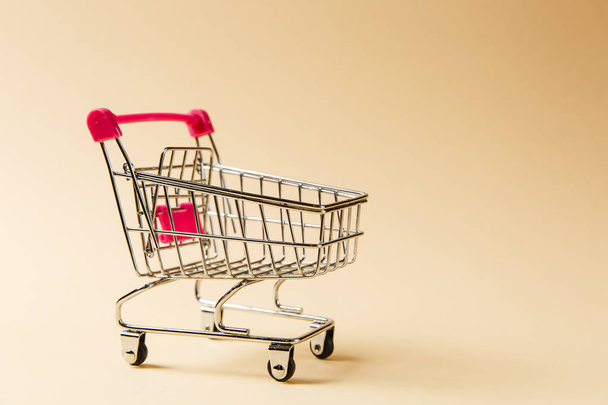 Close up of supermarket grocery push cart for shopping with black wheels and pink plastic elements on handle isolated on beige background. Concept of shopping. Copy space for advertisement - Foto, Imagen