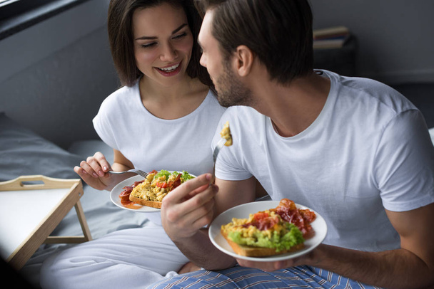 Улыбающиеся мужчина и женщина завтракают в постели
 - Фото, изображение