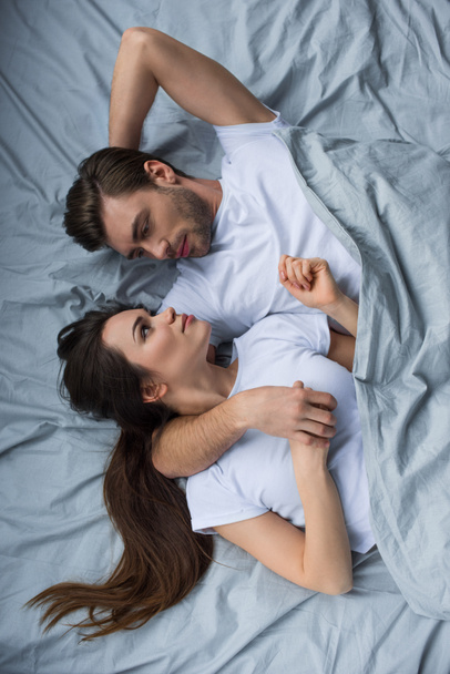 Smiling man and woman tenderly embracing while lying in bed - Fotografie, Obrázek