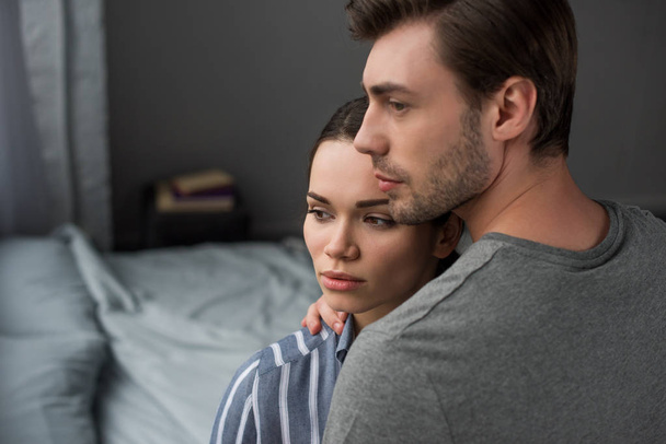 Young attractive couple hugging in bedroom and looking away - Fotografie, Obrázek