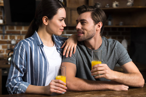 Attractive couple looking at each other and holding glasses with juice - Foto, afbeelding