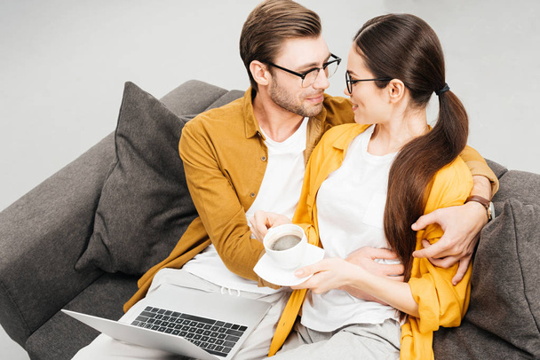 high angle view of couple with coffee and laptop embracing on couch at home - Fotó, kép