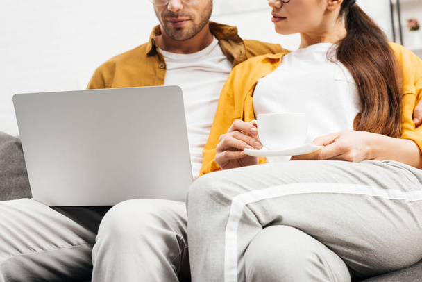Schnappschuss eines jungen Paares mit Kaffee und Laptop, das zusammen auf der Couch sitzt - Foto, Bild