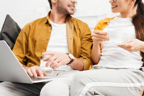 cropped shot of couple with coffee and laptop sitting on couch together - Foto, immagini