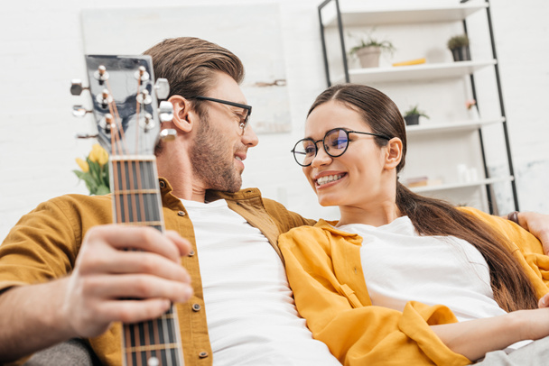 Paar mit Gitarre sitzt zu Hause auf Couch - Foto, Bild