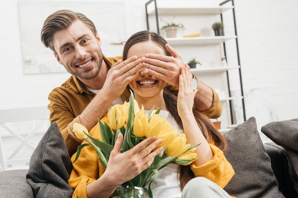 happy young man covering eyes of girlfriend and presenting her bouquet - Photo, image