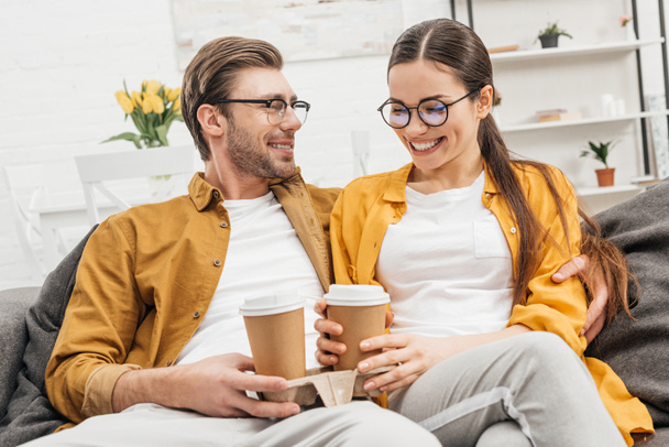 young happy couple drinking coffee from paper cups on couch - Foto, Imagem