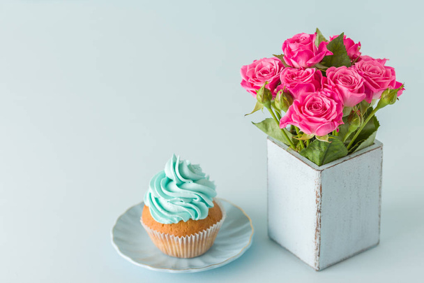 Μπλε παστέλ οριζόντια πανό με κάτοψη του διακοσμημένα με μπλε κρέμα cupcake και ροζ τριαντάφυλλα σε ρετρό shabby κομψό βάζο. - Φωτογραφία, εικόνα