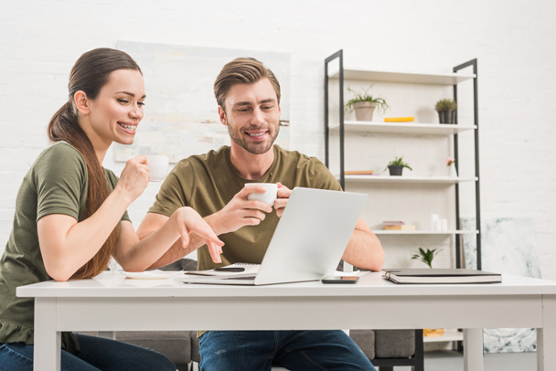 joven feliz pareja beber café y trabajar con el ordenador portátil juntos en casa
 - Foto, Imagen