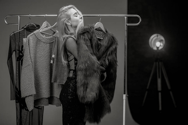 Jeune femme se tient à côté de rack avec cintres et rêves de manteau de fourrure. Image en noir et blanc
. - Photo, image