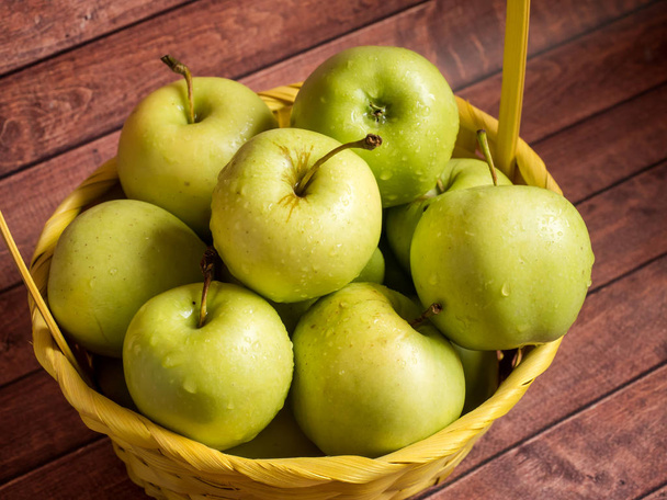 Green ripe apples in a wicker yellow basket - Φωτογραφία, εικόνα