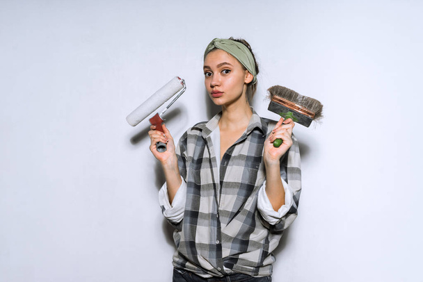 young girl in plaid shirt holding brush and roller for painting walls - Zdjęcie, obraz