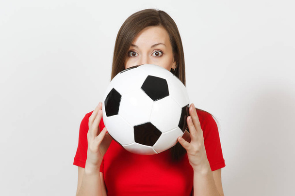 Beautiful European young woman, football fan or player in red uniform holding, hiding behind classic soccer ball isolated on white background. Sport, play football, health, healthy lifestyle concept. - Foto, afbeelding