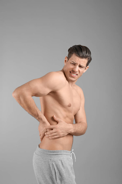 Young man suffering from flank pain on grey background - Photo, Image