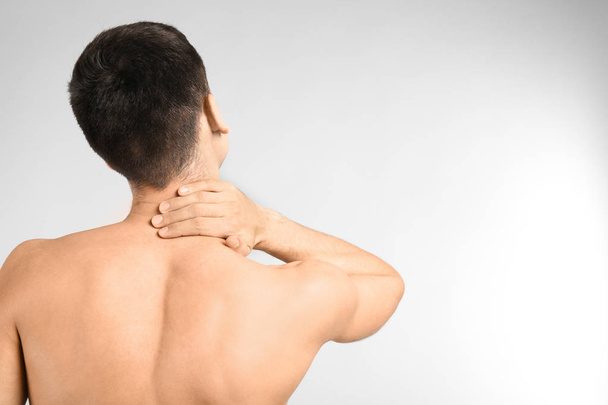 Junger Mann leidet an Nackenschmerzen vor hellem Hintergrund - Foto, Bild
