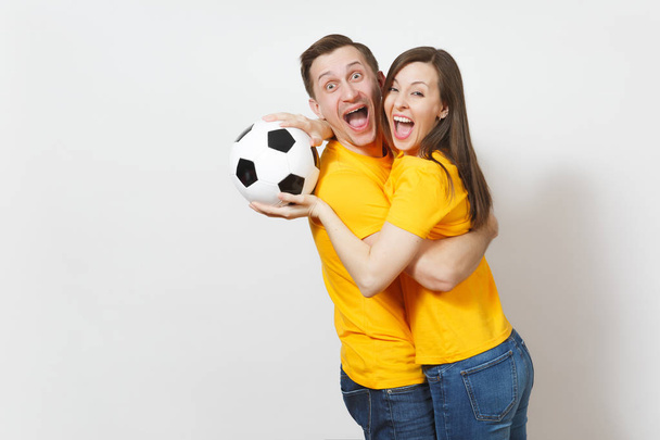 楽しいクレイジー陽気な感情的な若いカップル、女性、男、白い背景で隔離のサッカー ボールでサポート チーム元気づけるの黄色い制服のサッカーファン。スポーツ、レジャー、ライフ スタイルのコンセプト. - 写真・画像