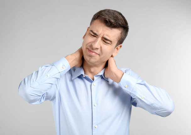 Young man suffering from neck pain on light background - Photo, image