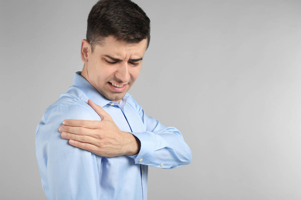 Young man suffering from pain in shoulder on light background - Foto, Bild
