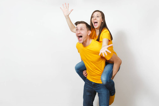Fun inspired young couple, woman sit on man piggyback, fans in yellow cheering favorite team, expressive gesticulating hands isolated on white background. Sport, family leisure, lifestyle concept. - Foto, afbeelding