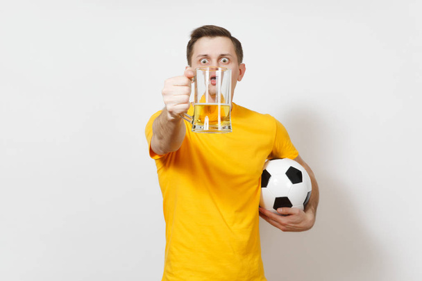Inspired young fun European man, fan or player in yellow uniform hold in front face pint mug of beer, soccer ball cheer favorite football team isolated on white background. Sport, lifestyle concept. - Foto, Imagem