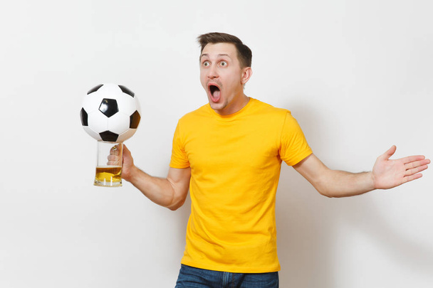 Вдохновлённый молодой веселый европейский мужчина, фанат или игрок в жёлтой форме держат кружку пива, футбольный мяч болеет за любимую футбольную команду, изолированную на белом фоне. Спорт, игры, концепция образа жизни
. - Фото, изображение