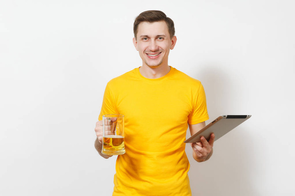Молоді європейських усміхнений чоловік у жовта маєчка, джинси, проведення пінта кухоль пива, планшетний ПК комп'ютер ізольовані на білому тлі. Студент спосіб життя, відпочинку та технології концепції. - Фото, зображення