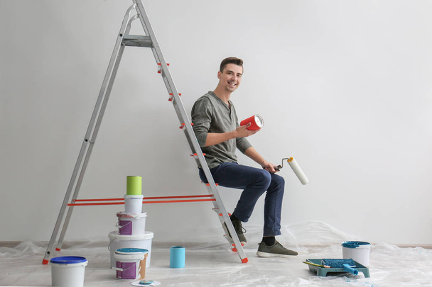 Male decorator sitting on ladder in empty room - Fotoğraf, Görsel