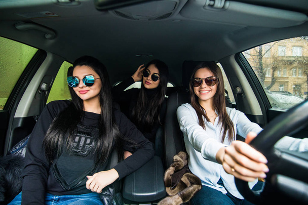 три дівчини в сонцезахисних окулярах, що їздять в кабріолеті і розважаються
 - Фото, зображення