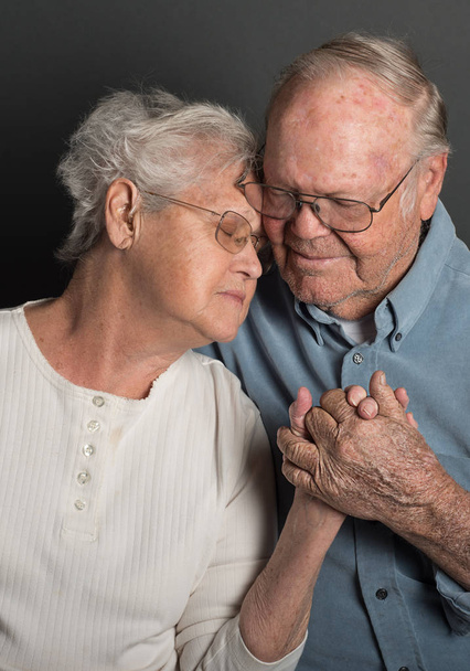 Senior couple holding hands in a tender loving embrace in monochrome, both wearing glasses, man unshaven - Fotó, kép