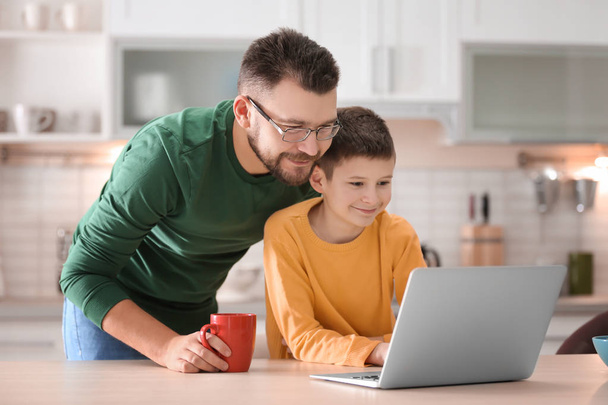 Little boy and his dad using laptop in kitchen - Zdjęcie, obraz